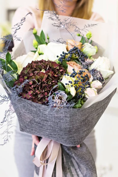 Beautiful bouquet in with roses and dark purple hydrangea. Modern, stylish bouquet in female hands