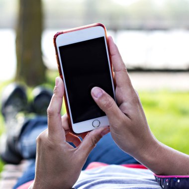 Bir şezlong nehrin arka planı kadının elinde cep telefonu. Telefon, şezlong, Yeşil çimenler, nehir. Dinlenme zamanı. Tatil, doğada telefon üzerinde çalışmak.