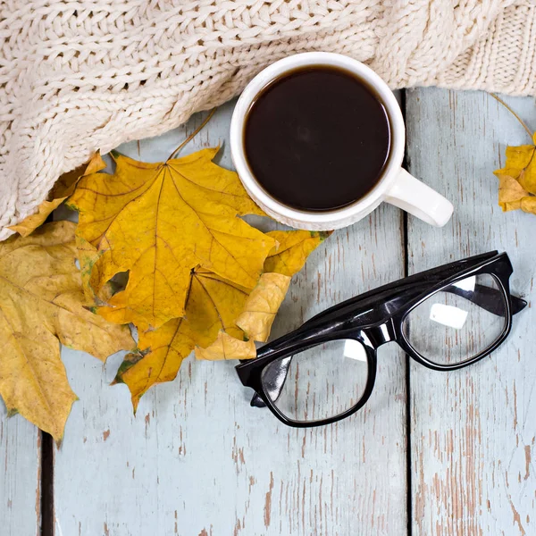 Teplá bílá pletená kostka, káva, telefon, brýle, podzimní listy na dřevěné pozadí. — Stock fotografie
