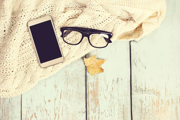 Chaud blanc tricoté plaid, café, téléphone, lunettes, feuilles d'automne sur un fond en bois . — Photo