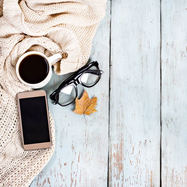Warm white knitted plaid, coffee, phone, glasses, autumn leaves on a wooden background. — Stock Photo, Image