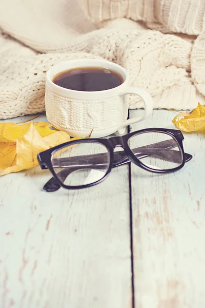 Warme witte gebreide Plaid, koffie, telefoon, bril, herfst bladeren op een houten achtergrond. — Stockfoto