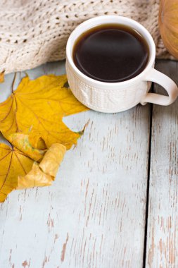 Sonbahar rahatlığı. Sonbahar sakin bir hayattır. Kahve, ekose ve sonbahar yaprakları mavi ahşap bir masada. Bir fincan aromatik kahve, sıcak ekose, kitap ve sonbahar yapraklı kompozisyon.