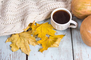 Sonbahar rahatlığı. Sonbahar sakin bir hayattır. Kahve, ekose ve sonbahar yaprakları mavi ahşap bir masada. Bir fincan aromatik kahve, sıcak ekose, kitap ve sonbahar yapraklı kompozisyon.