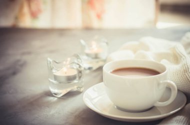 Oturma odasının iç kısımlarında hala hayat detayları var. Masada bir fincan kakao, mumlar ve örgü battaniye. Sıcak sonbahar ya da kış konsepti.