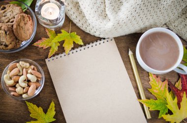 Boş kahverengi defter ile örgü battaniye, bir fincan sıcak çikolata ve ahşap masa snacks. Şükran günü kavramı. Sonbahar natürmort. Rahat sonbahar ruh hali. Kopya alanı.