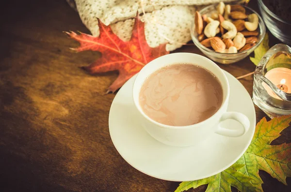 A cup of hot cocoa, nuts, cookies, candle and knitted plaid on a rustic wooden table. Cozy autumn mood, warm autumn.