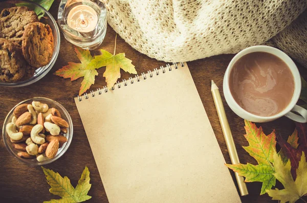 Blank brown notebook with knitted blanket, a cup of hot cocoa and snacks on wooden table. Thanksgiving day concept. Autumn still life. Cozy autumn mood. Copy space.