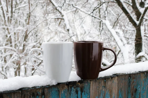 Cozy winter still life: Two Cups of Hot Coffee or Tea on a Snow Covered Terrace. Frosty winter day in forest. Christmas Holidays. Winter Cozy Background