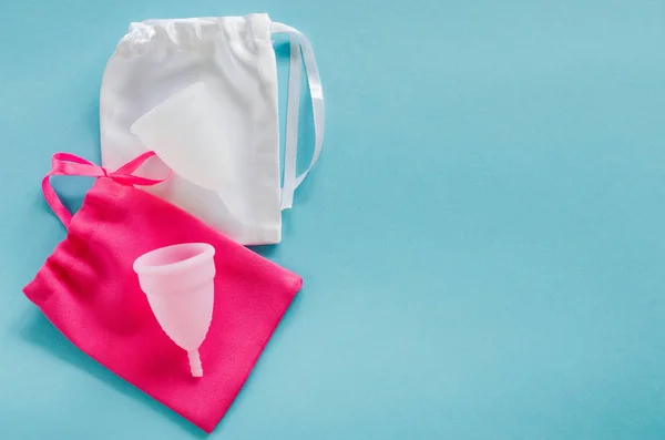 Pembe ve beyaz adet su bardağı elinde çanta mavi arka plan, kadın Hijyen Intimate dönem ürünleri, üstten görünüm