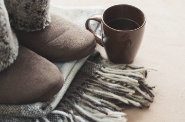 Sıcak ev kıyafetleri. Yünlü ekose kumaş, terlik ve bir fincan sıcak içecek..
