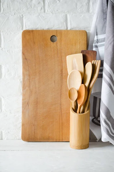 Simple rustic kitchenware: wooden or bamboo cutlery, towel and cutting board in interior of white kitchen. Rustic style. Home Kitchen Decor.