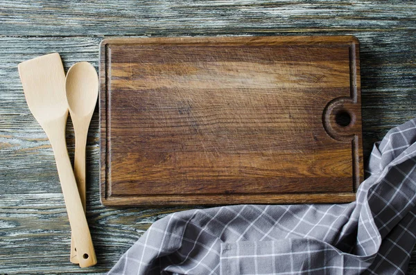 Culinary background with rustic kitchenware: wooden or bamboo cutlery, vintage cutting board and towel against vintage wooden background. Rustic style. Home Kitchen Decor. View from above.