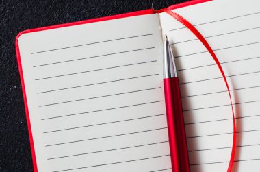 Koyu arka plan üzerinde kırmızı kalemile boş açık kırmızı defter. Metin için boş kağıt.