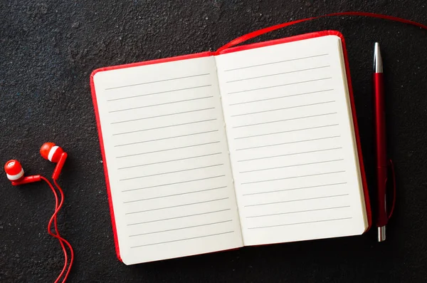 Порожній червоний блокнот з червоною ручкою та навушниками на темному тлі. Порожній папір для тексту . — стокове фото