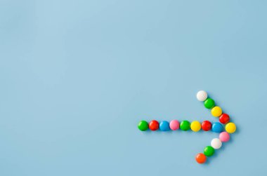 Mavi arka planda renkli sır ile çikolata şeker işaretçi ok.