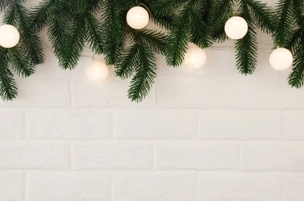 Λευκός τοίχος από τούβλα με κλαδιά ελάτης και χριστουγεννιάτικα φώτα με τη μορφή λευκών σφαιρών. — Φωτογραφία Αρχείου