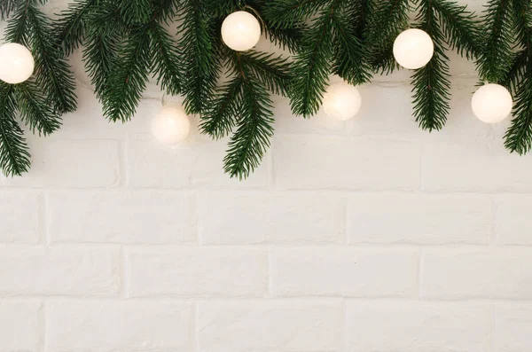 Köknar dalları ve beyaz toplar şeklinde Noel ışıkları olan beyaz tuğla duvar..