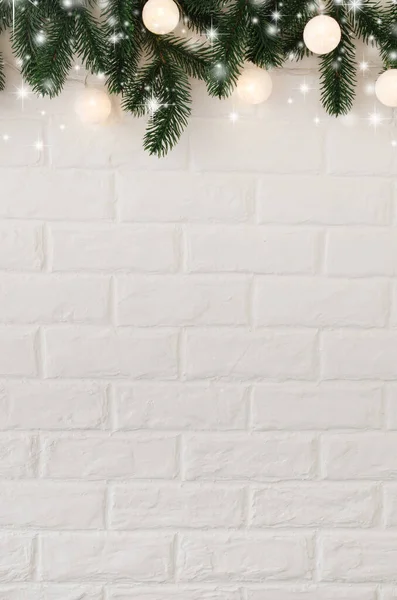 Köknar dalları ve beyaz toplar şeklinde Noel ışıkları olan beyaz tuğla duvar..