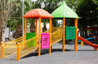Yeşil ağaçlarla çevrili parktaki renkli çocuklar oyun parkı aktiviteleri.