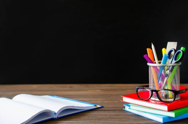 Okula dönelim. Kitap yığını, okul malzemeleri ve kara tahta üzerinde gözlük. Eğitim konsepti. Boşluğu kopyala