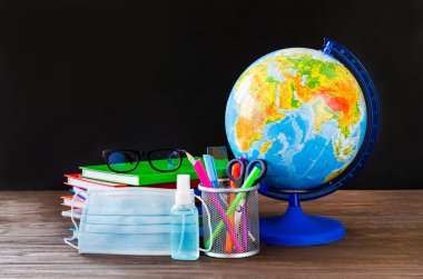 Karantina sırasında okula dönmek. Tıbbi maskeli okul malzemeleri ve karatahta arka planında dezenfektan. Eğitim konsepti. Boşluğu kopyala