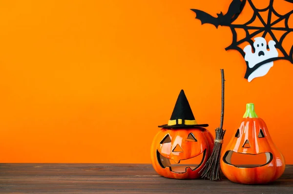 Halloween holiday background with jack lanterns pumpkin, broom and witch hat on wooden table. Halloween holiday celebration.