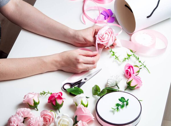 Flower shop: A girl makes a bouquet of roses in a round box. Close-up of hands. Horizontal shot.