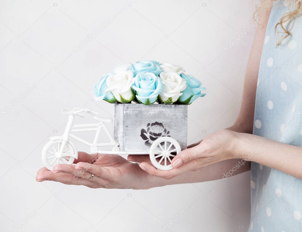 Wedding handmade decor: The girl holds a small bouquet of roses in her hands in a decorative box in the form of a bicycle. Close-up of hands. Light background.