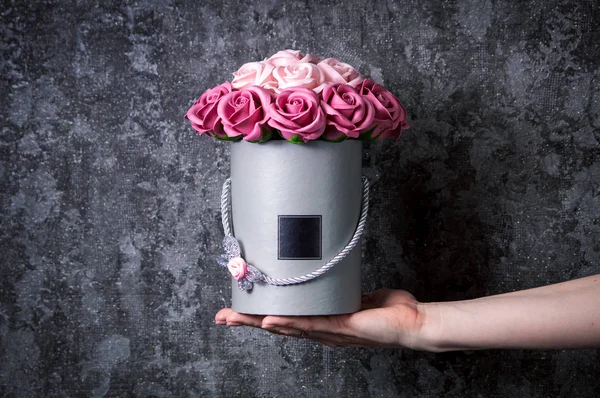 Decoración de la boda: Un ramo de rosas rosadas en una caja de sombrero gris en las manos de una chica sobre un fondo gris . — Foto de Stock