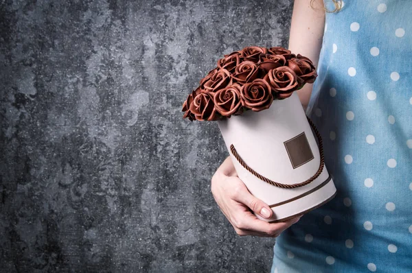 Una chica con un vestido azul sostiene una caja de jerez con un ramo de rosas marrones en sus manos . — Foto de Stock