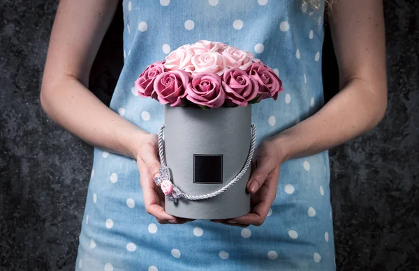 Una chica con un vestido azul sostiene una caja de jerez con un ramo de rosas rosadas en sus manos . — Foto de Stock