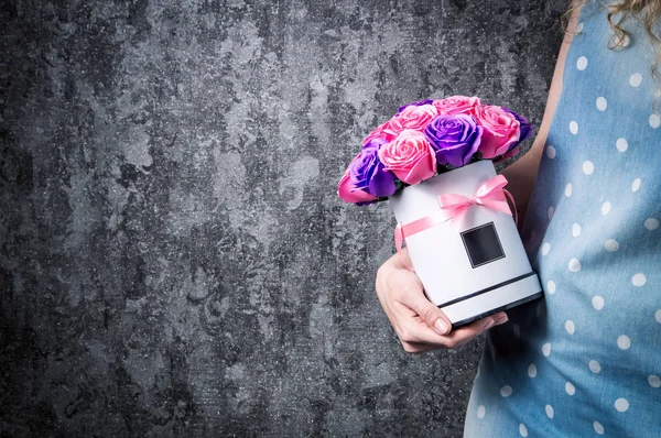 Una chica con un vestido azul sostiene una caja de jerez con un ramo de rosas en sus manos . — Foto de Stock