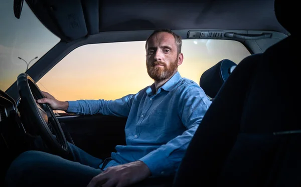 Un homme barbu en chemise conduisant une voiture avec un salon bleu . — Photo