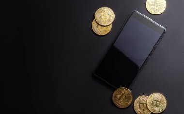 Kripto-para kazanç: altın paralar bitcoin ve karanlık bir arka plan üzerinde smartphone. Yatay çerçeve. Yakın çekim.