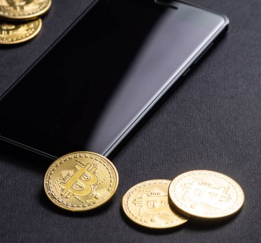 Kripto-para kazanç: altın paralar bitcoin ve karanlık bir arka plan üzerinde smartphone. Kare kare. Yakın çekim.