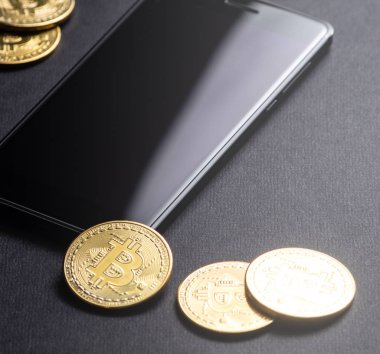 Kripto-para kazanç: altın paralar bitcoin ve karanlık bir arka plan üzerinde smartphone. Kare kare. Yakın çekim.