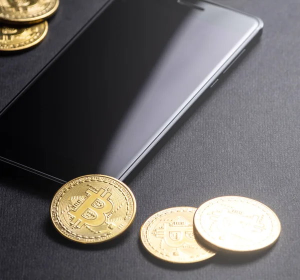 Kripto-para kazanç: altın paralar bitcoin ve karanlık bir arka plan üzerinde smartphone. Kare kare. Yakın çekim.