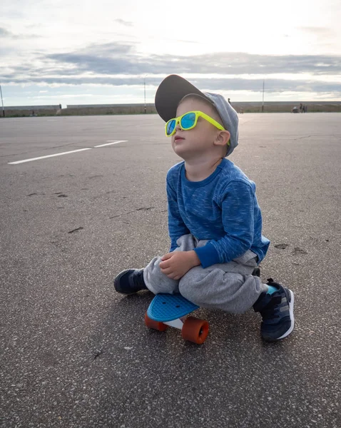 Straat sport voor kinderen: een jongetje in een pet en zonnebril ging zitten op een blauw bord cent om te ontspannen. — Stockfoto