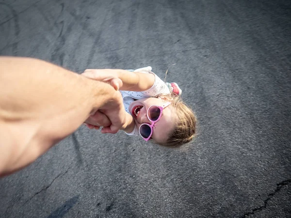 Een meisje in roze zonnebril vasthouden aan haar vaders hand. De papa cirkels zijn dochter om hem heen. — Stockfoto
