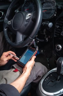 Araba hataları tanılama: gri giysiler içinde bir elektrikçi arabalar iç oturma ve bir taşınabilir otomatik tarayıcı Obd2 arayüzü ile trouble kodları okuma.