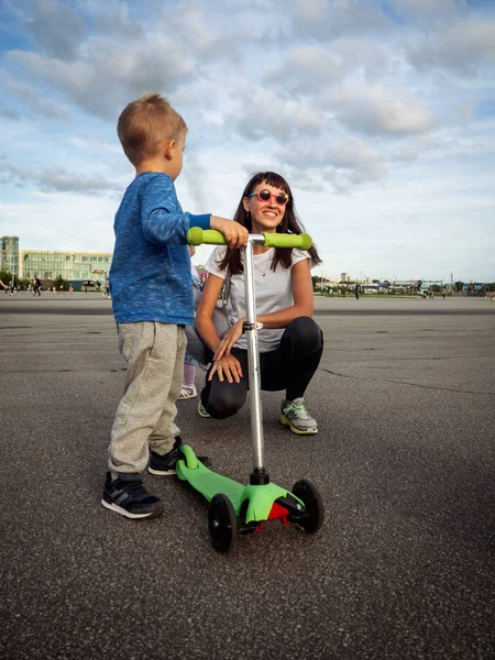 Straat sport: de zoon zijn moeder laat zien hoe hij klapschaatsen op de scooter. Actieve rust in de stad. Verticaal schot. — Stockfoto
