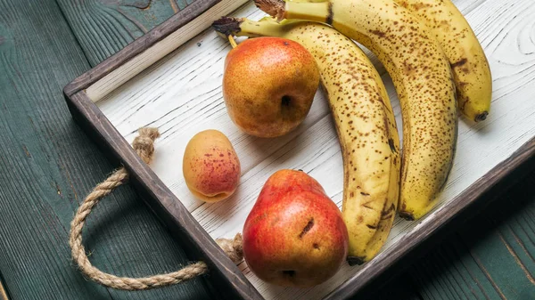 Beyaz ahşap tepsi üzerinde taze meyve: banatas, armut, kayısı. Kırsal ayar. Üstten görünüm. Kopya alanı