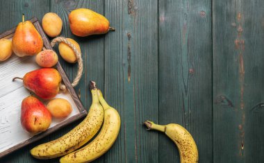 Beyaz ahşap tepsi üzerinde taze meyve: banatas, armut, kayısı. Kırsal ayar. Üstten görünüm. Kopya alanı