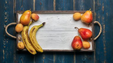 Beyaz ahşap tepsi üzerinde taze meyve: banatas, armut, kayısı. Kırsal ayar. Üstten görünüm. Kopya alanı