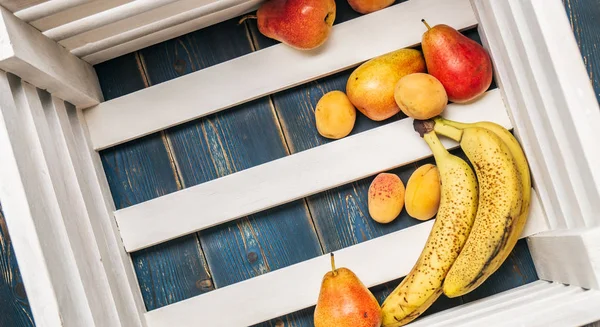 Sağlıklı gıda: Olgun taze muz, armut, kayısı bir ahşap kutu dibinde. Kopya alanı