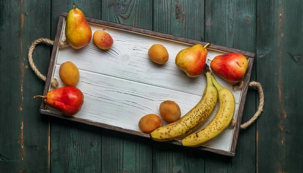 Beyaz ahşap tepsi üzerinde taze otantik meyve: banatas, armut, kayısı. Kırsal ayar. Üstten görünüm. Kopya alanı