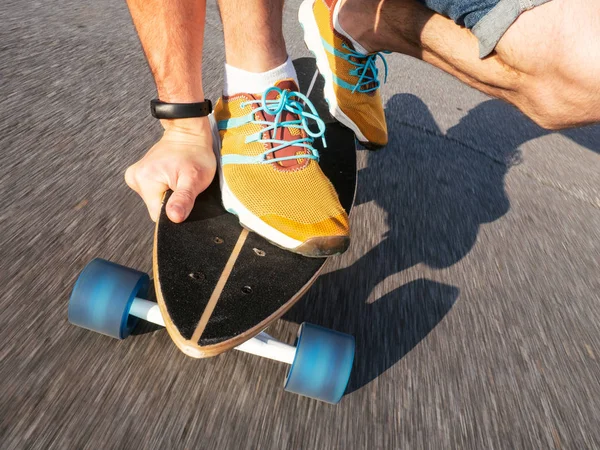 Street high-speed sports: A guy in yellow sneakers is rolling on a longboard along the road. Asphalt is smeared with speed. Close-up of legs and skateboard-pintail.
