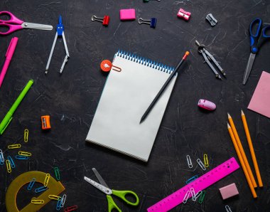 Okul malzemeleri okul için: Not defteri, kalemler, pembe cetvel, gri bir tablo üzerinde dağınık pergel. Üstten görünüm.