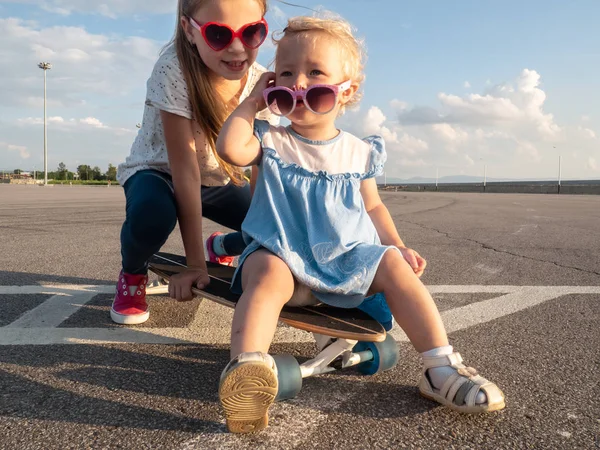 Street sports: two dvoichki in sunglasses sit on one large longboard in bright sunny weather. Close-up.